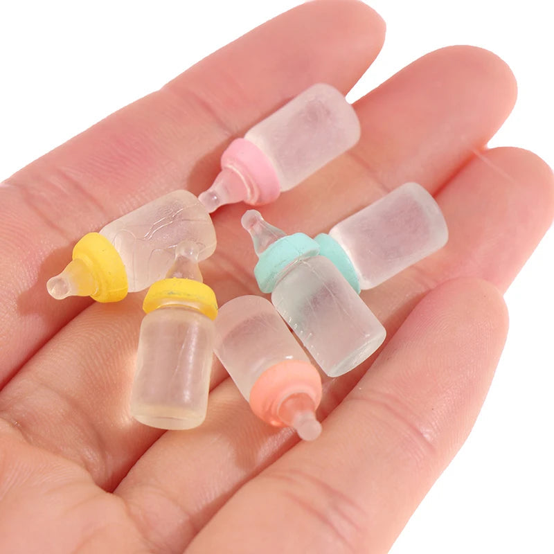 Miniature baby bottles with colorful caps, perfect for dollhouse nurseries, displayed on a hand for size reference.