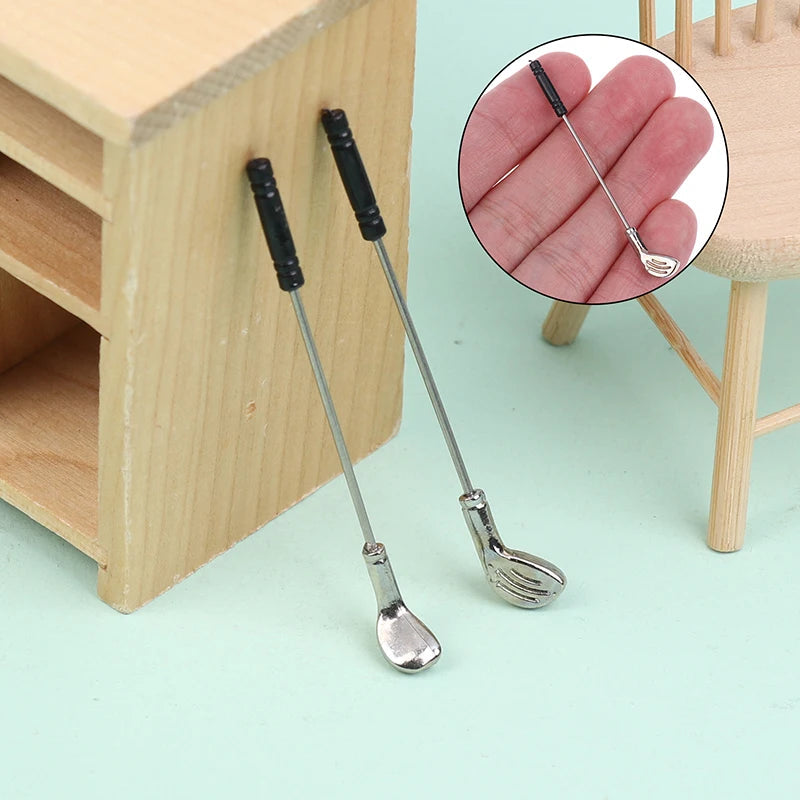 Miniature golf club set for dollhouses, featuring two detailed metal clubs with black grips, perfect for tiny golf enthusiasts.