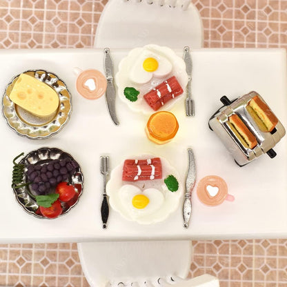 Miniature breakfast set with eggs, toast, cheese, and fruit on a dollhouse kitchen table, featuring 16 detailed pieces.