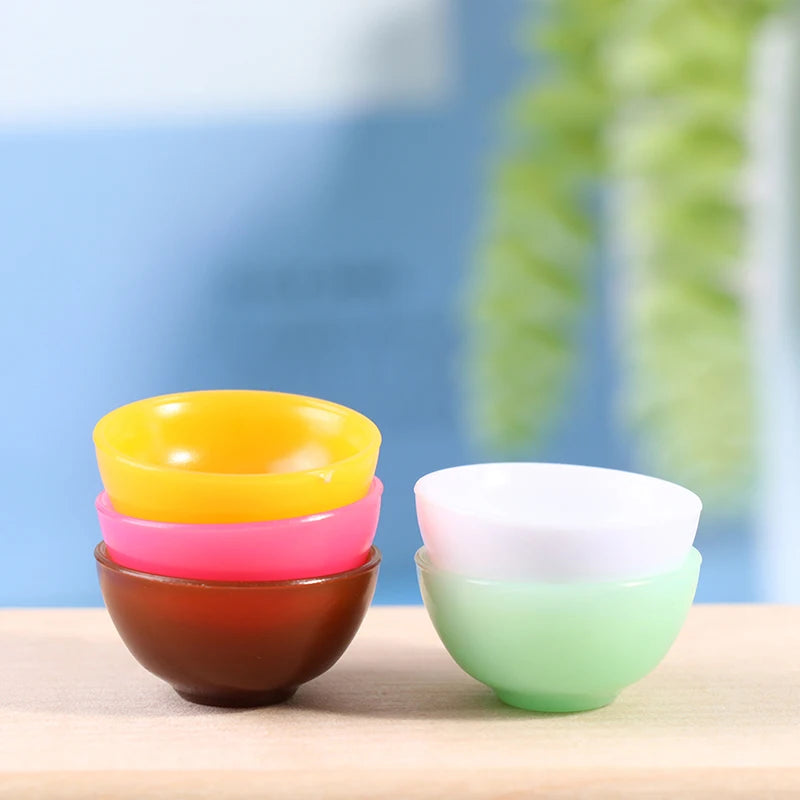 Colorful miniature dollhouse bowls stacked neatly, featuring vibrant yellow, pink, brown, white, and green hues.