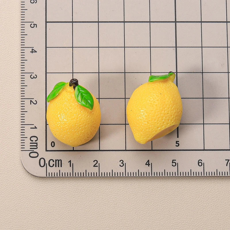 Miniature 1:12 dollhouse resin lemons with green leaves on a grid background for scale, perfect for dollhouse decor.